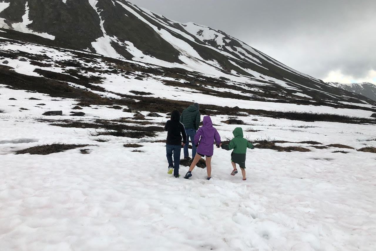 A family walking across deep snow at Hatcher Pass below a snowy mountain