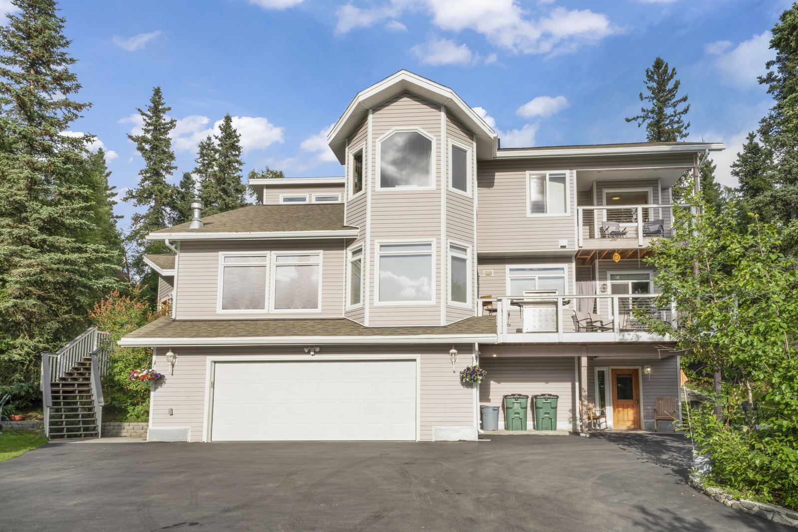 Front of Hillside Haven: three-story house with decks and a two-car garage among spruce trees