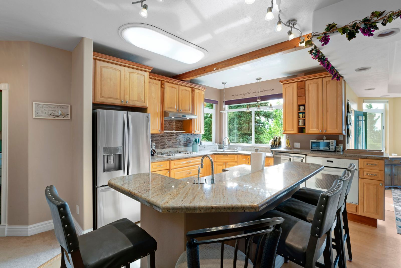 Kitchen with granite island, bar stools, stainless refrigerator and maple cabinets