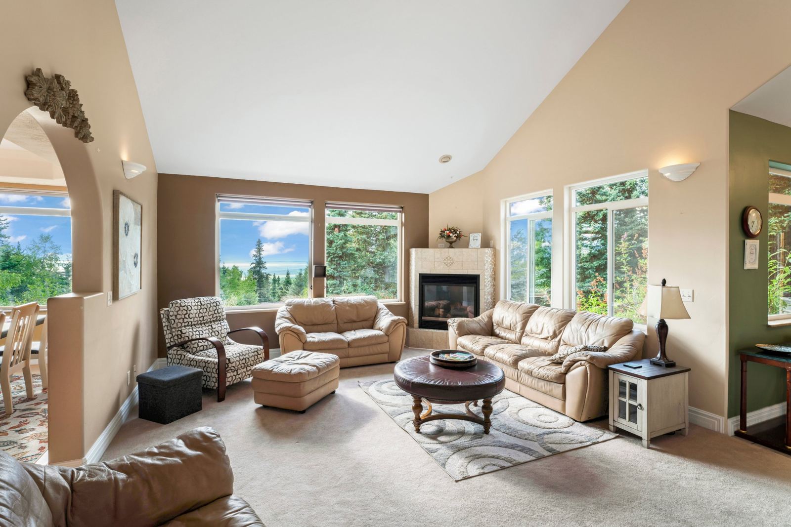 Living room at Hillside Haven with leather sofas, a corner gas fireplace and tall windows facing Cook Inlet