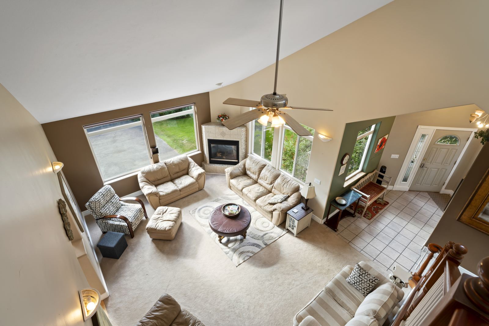 Living room seen from the stairs: sofas, fireplace, ceiling fan and tall windows