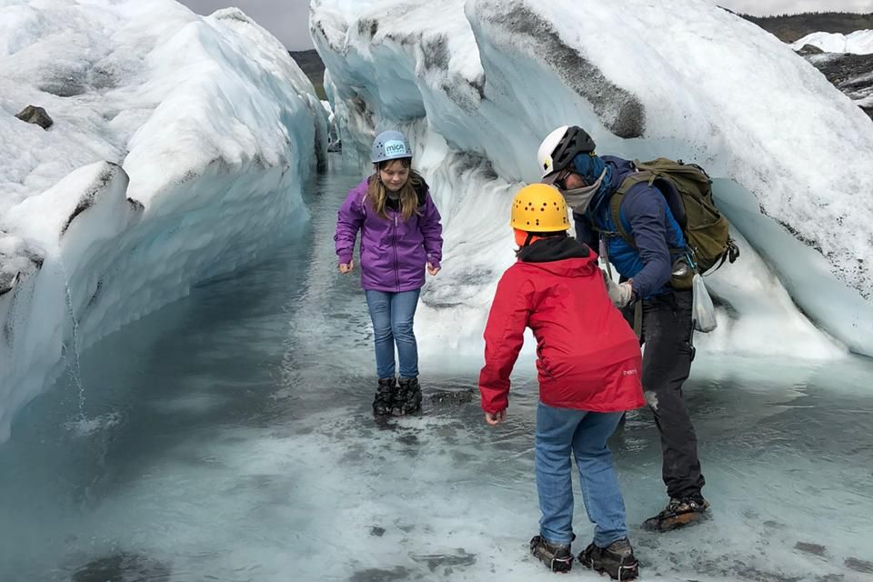 Kids in helmets and crampons walking through blue ice on the Matanuska Glacier with a guide