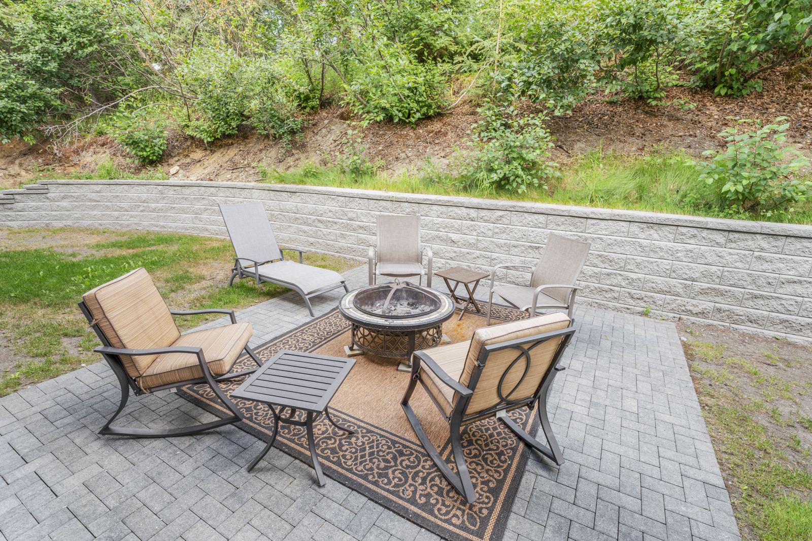 Paver patio with a fire pit and lounge chairs below a garden wall