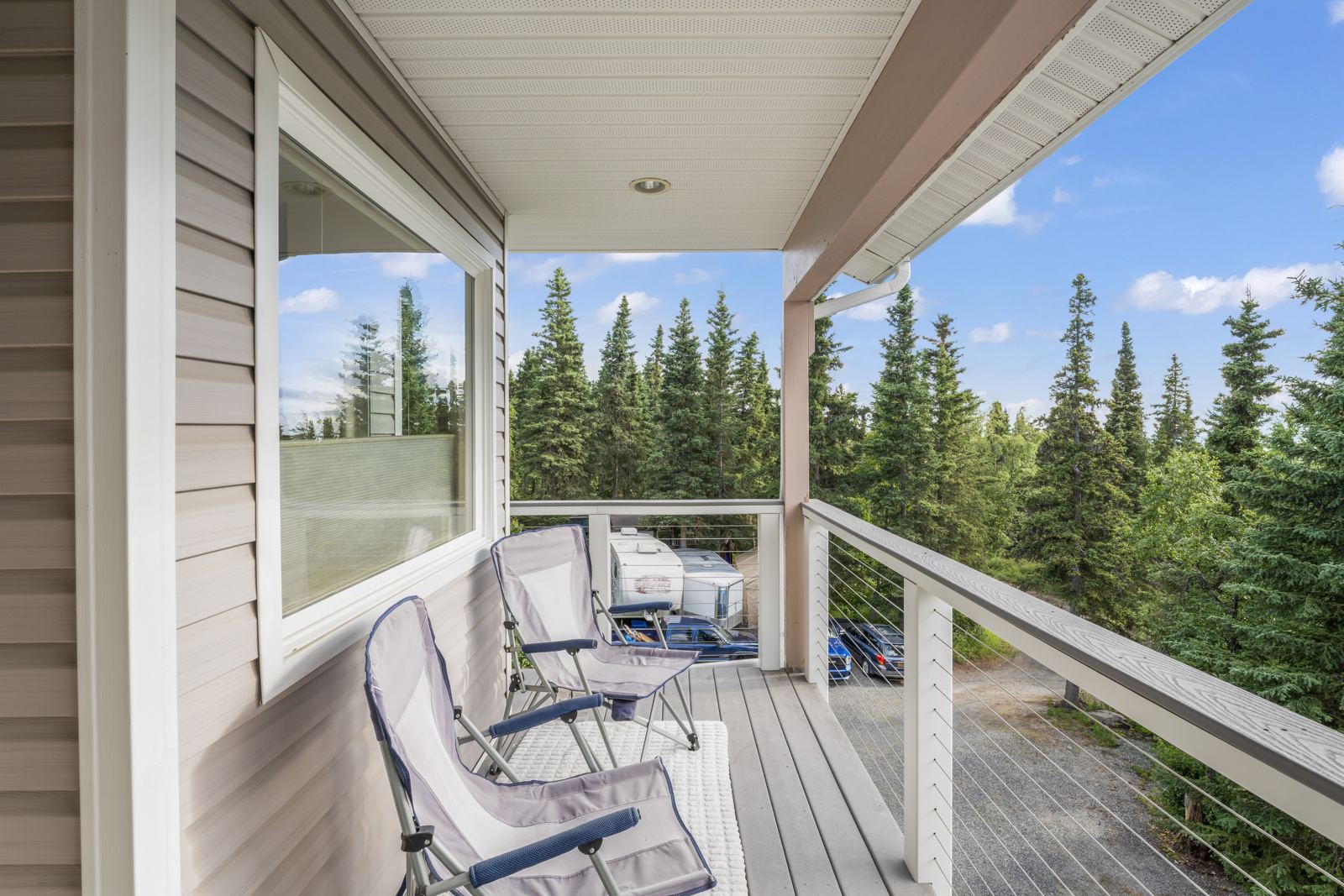 Private deck off the primary suite with chairs and a view over spruce trees