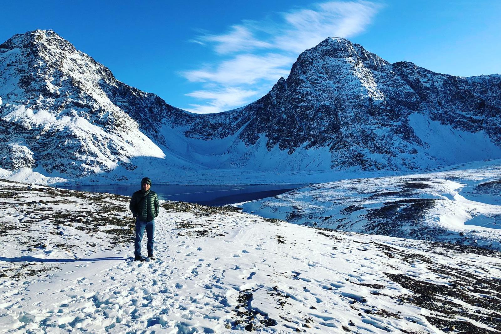 A hiker on snowy tundra below jagged peaks at Rabbit Creek Lake in Chugach State Park