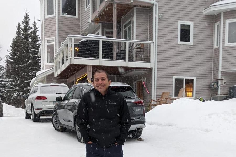 Snow falling at the front of the house, with cars in the snowy driveway